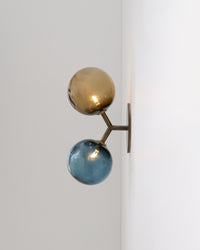Wall-mounted lamp with two glass spheres, one gold and one blue, on a white wall.