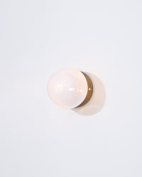 Wall-mounted light fixture with a white globe and gold trim on a light gray background