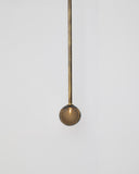 Minimalist pendant light with a spherical brown glass shade and brass rod on a white background