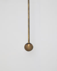 Minimalist pendant light with a spherical brown glass shade and brass rod on a white background
